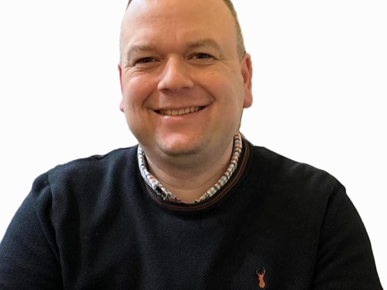 Smiling professional man in a black sweater and collared shirt for a business headshot.