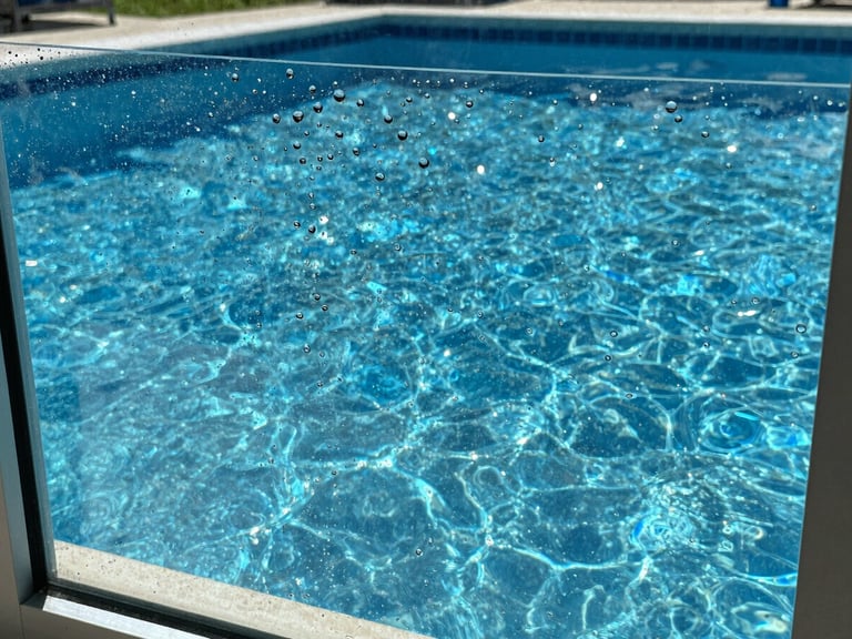 Close-up of clean water beads on a pristine glass window pane overlooking a sparkling blue pool cage, bright direct Florida sunlight