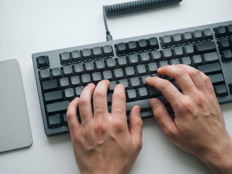 Close-up of hands typing on a mechanical keyboard on a clean white desk, soft overcast light, cool slate tones, 35mm