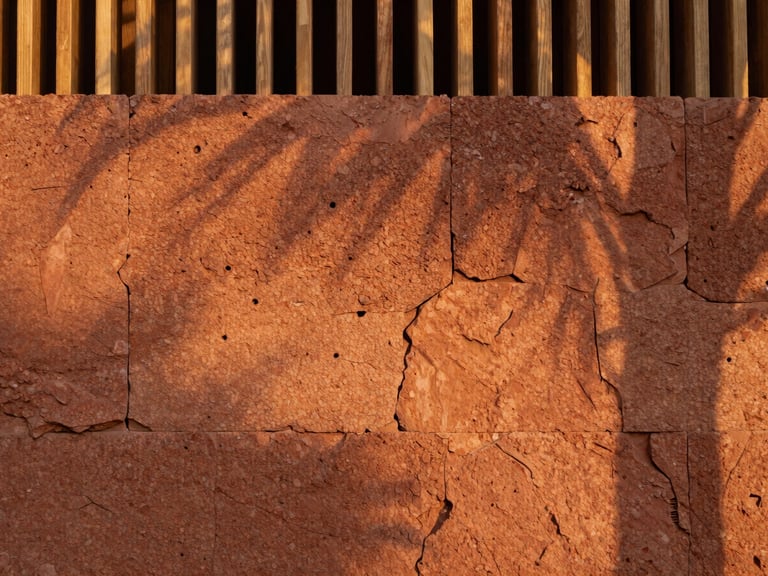 Close-up architectural detail of a porous laterite stone wall, warm terracotta tones, soft diffused golden-hour light filtering through a timber screen.