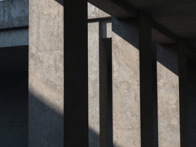 Architectural editorial photography of stark concrete pillars casting sharp geometric shadows under high-contrast overcast daylight, desaturated navy tones, 35mm.