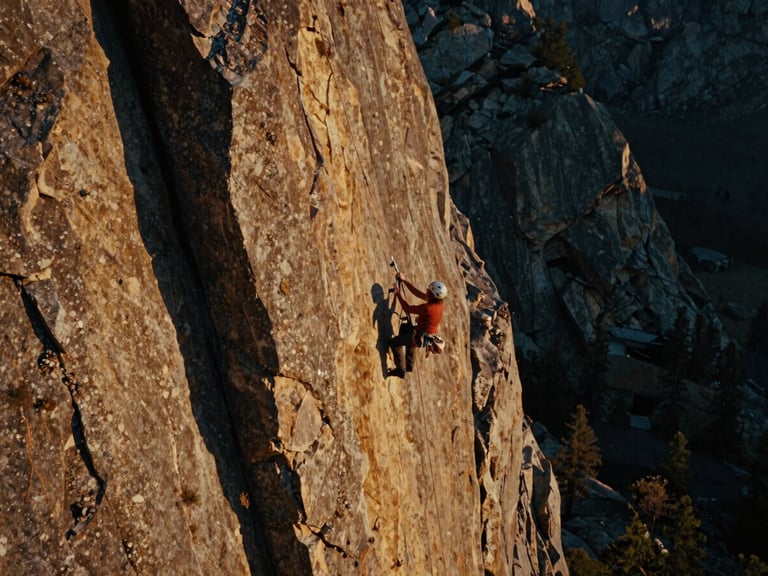 Dramatic wide shot of a climber ascending a rock face in the Wasatch Front, golden hour lighting, cinematic film grain, product visible.