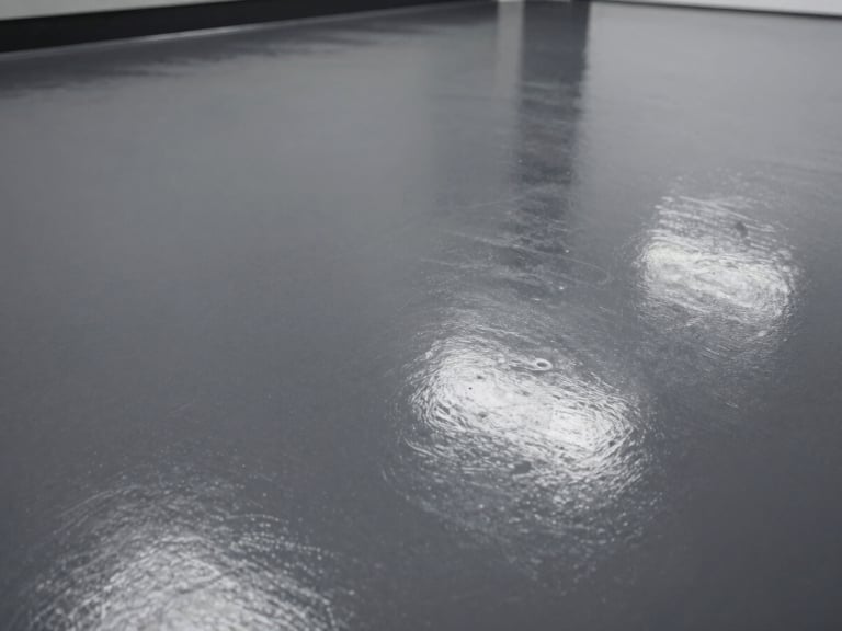 Close-up, high-contrast shot of a dark gray epoxy floor, showing a seamless, reflective surface under bright industrial lighting, low angle.