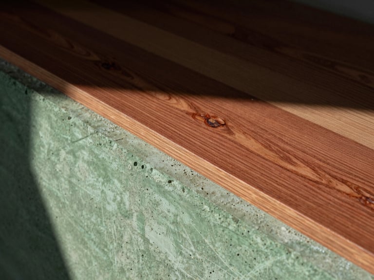 Extreme close-up of raw concrete and walnut wood material transitions in an empty sunlit interior, deep shadows, 35mm.