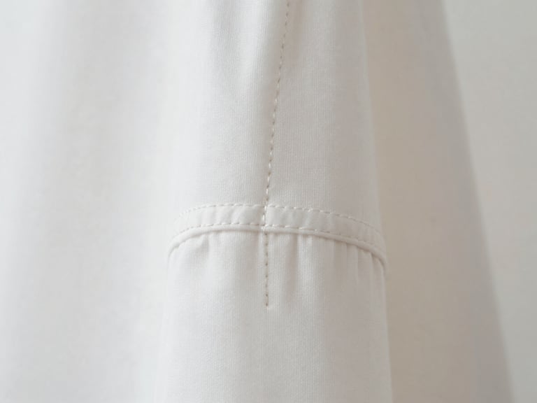 Macro close-up of a perfectly stitched seam on a white garment, showcasing the clean lines and craftsmanship, soft studio lighting.