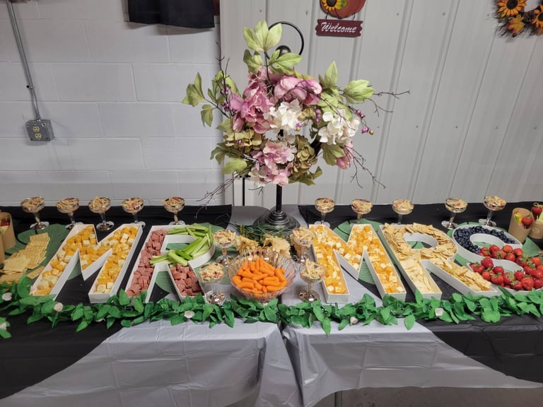 Wedding appetizer table with MR AND MRS letter trays filled with cheese, meat, fruit, and snacks.