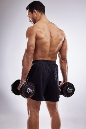 Rear view of a muscular man holding heavy dumbbells for back and shoulder strength training.