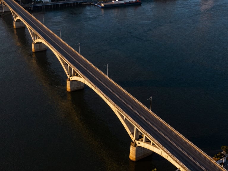 High-angle panoramic shot of a massive concrete bridge spanning a wide river, golden hour lighting, cinematic architectural photography