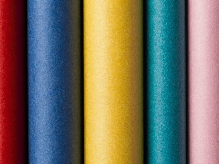 Tight macro shot of a stack of seamless paper rolls in various colors, textured surface, sharp high-contrast studio light, rich saturated colors, crisp depth of field, 35mm.
