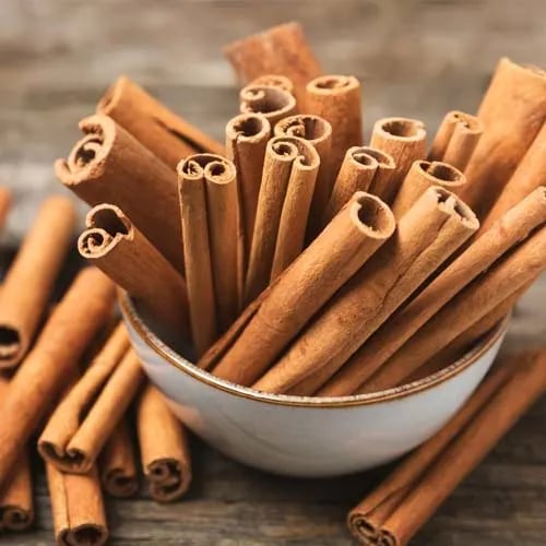 A small ceramic bowl filled with organic cinnamon sticks on a rustic wooden table.