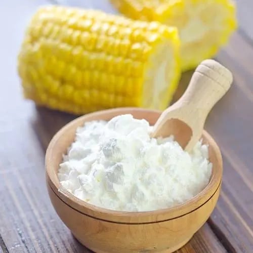 White organic cornstarch powder in a wooden bowl with a scoop next to fresh corn on the cob.