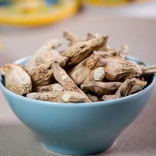 A blue bowl filled with dried ginger root pieces, a common spice used for cooking and herbal tea.
