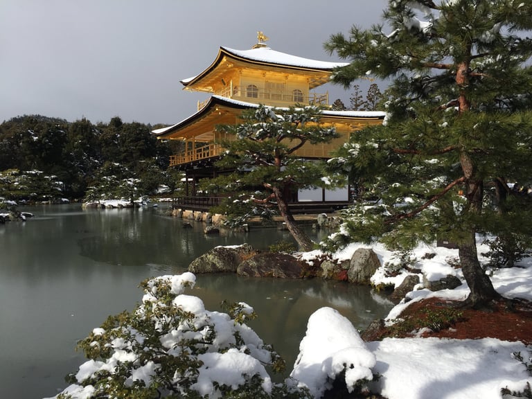 Kinkaku-ji, the Golden Pavilion temple in Kyoto, dusted with snow above a frozen pond.