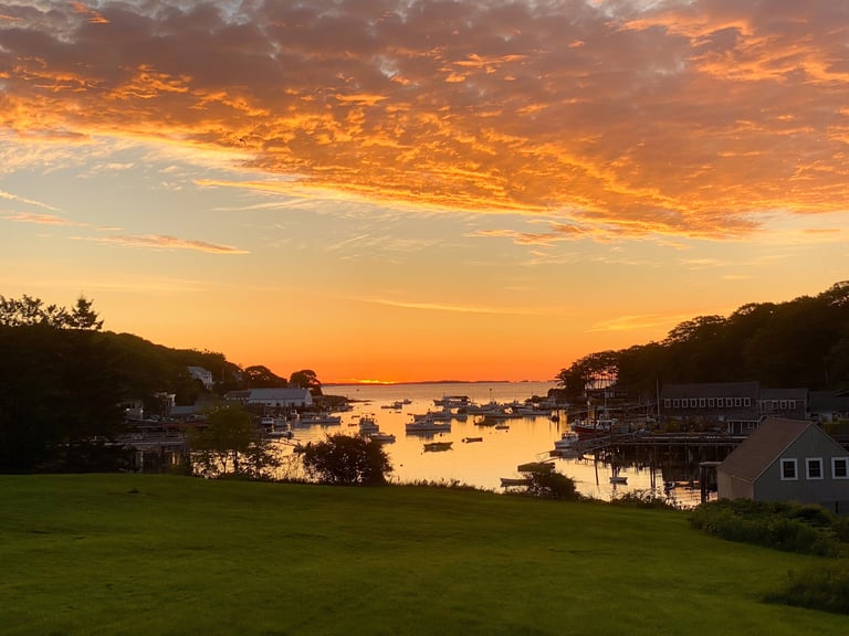 A small Maine fishing harbor at sunrise, fishing boats at their moorings under a glowing orange sky.