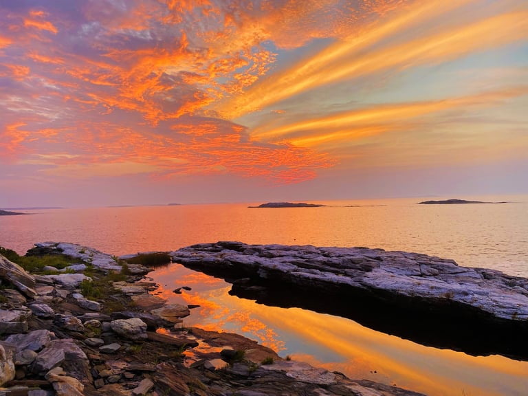 Sunrise over a rocky Maine coastline with orange sky reflected in tidal pools among the rocks.