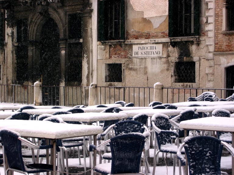 Snow-covered café tables and chairs in an empty Venetian piazza.