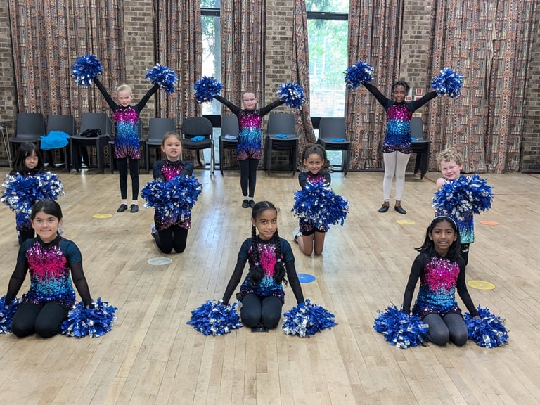 Young cheerleaders in sequined uniforms posing with blue pom poms during a dance class performance.