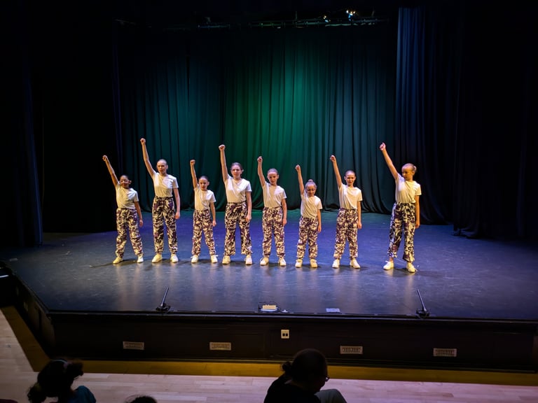 Young dancers performing a street dance routine on a stage in purple camouflage trousers.