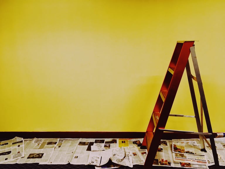 intérieur avec un mur jaune, avec un escabot en bois marron, ave du papier journal au sol 