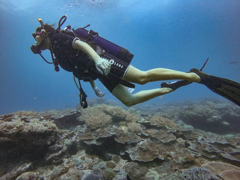 Scuba diver with fins swimming over a vibrant coral reef in clear blue ocean water.