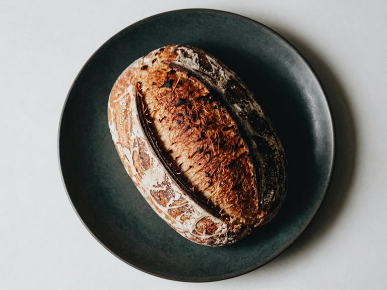 Overhead flat lay of a minimalist Scandinavian-style sourdough bread on a dark ceramic plate, natural side-light casting moody shadows, matte finish, 35mm film style.