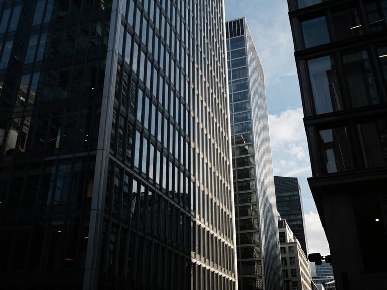 Extreme wide-angle environmental shot of modern London steel-and-glass skyscraper sliced by sharp morning sunlight and deep obsidian shadows.