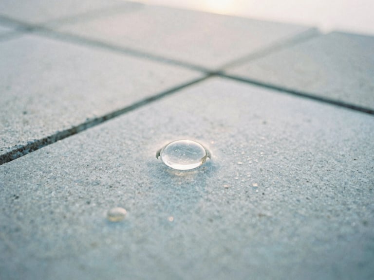 Macro photograph of clean water reflecting soft morning light on a light gray stone tile, shallow depth of field, 35mm