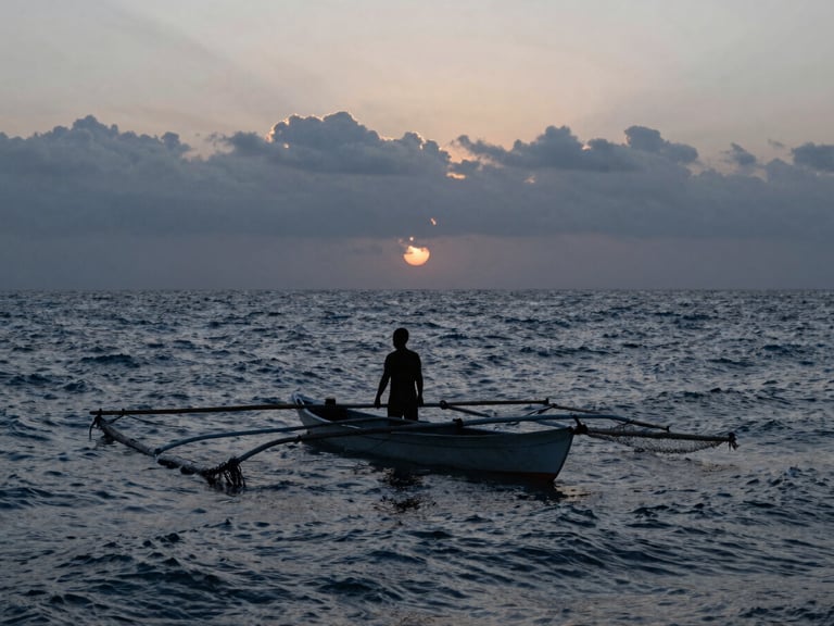 Pescador local en una panga con redes de pesca al amanecer en San Quintín, silueta dramática contra el sol naciente sobre el mar agitado.