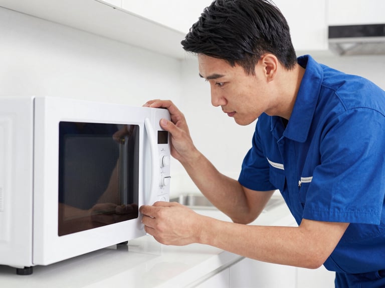 Medium shot of a uniformed technician carefully inspecting an IFB microwave oven's internal components, focused expression, clean home kitchen background, sharp focus.