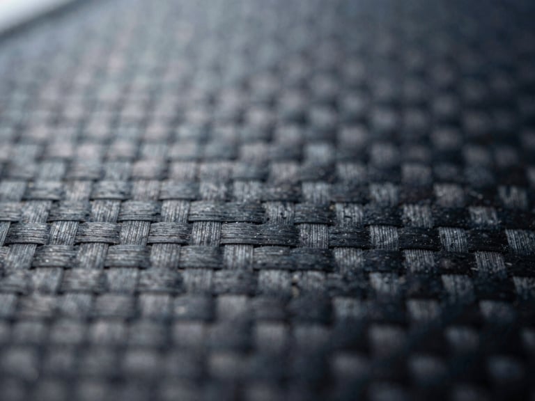 Macro shot of a damaged carbon fiber weave, high-contrast industrial lighting, desaturated steel and deep blue tones, 35mm
