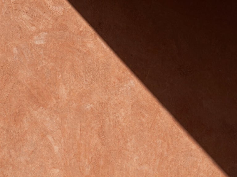 An architectural detail of raw plaster meeting warm terracotta clay, sharp diagonal shadow, minimal composition