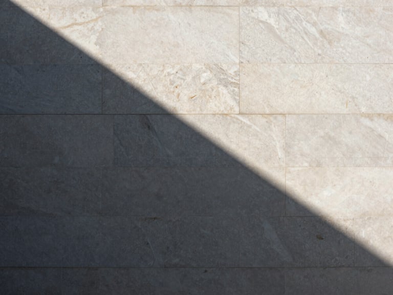 Direct sunlight casting sharp geometric shadows on a monolithic travertine wall, architectural elevation, high-contrast, minimalist.