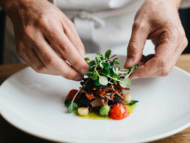 Close-up of a chef's hands plating a vibrant dish with microgreens, soft natural side lighting, shallow depth of field