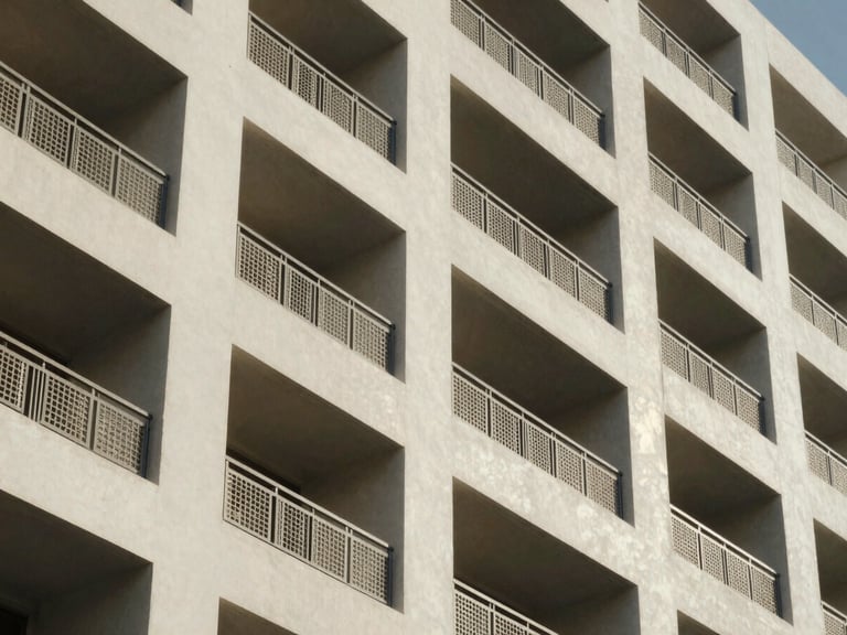 Close architectural detail of a mid-rise residential building façade in Abu Dhabi, north-facing diffused daylight, geometric balcony grilles casting shallow shadows on off-white render, upper floors receding slightly out of focus — no people, no staging
