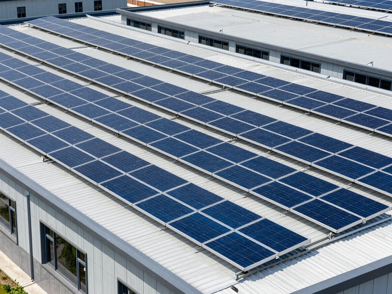 Wide environmental shot of commercial solar panels installed on a modern flat facility roof, clean architectural lines, crisp daylight, sharp geometric composition.
