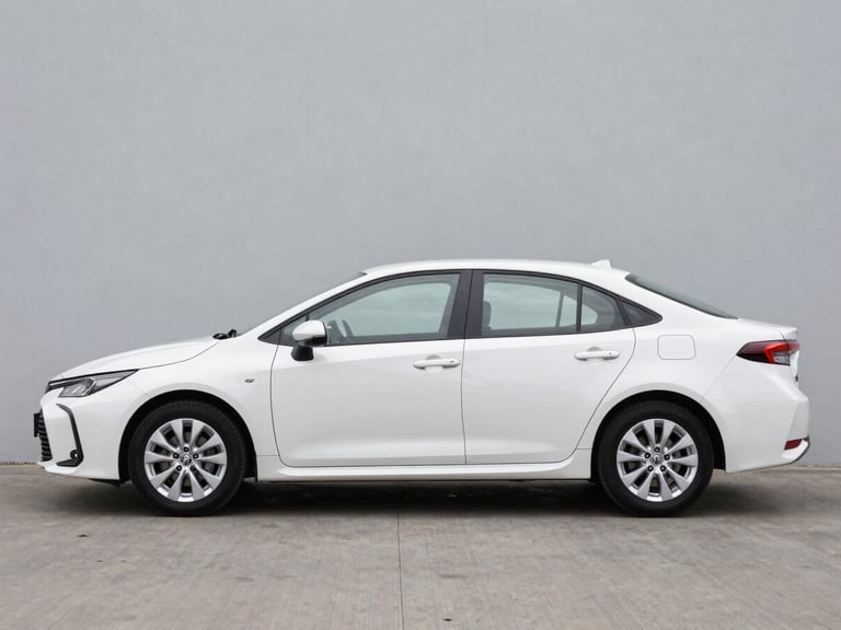 Full-side view of a white Toyota Corolla sedan parked on a clean neutral grey surface, natural overcast daylight, car centered in frame showing full profile, no people, studio-clean background