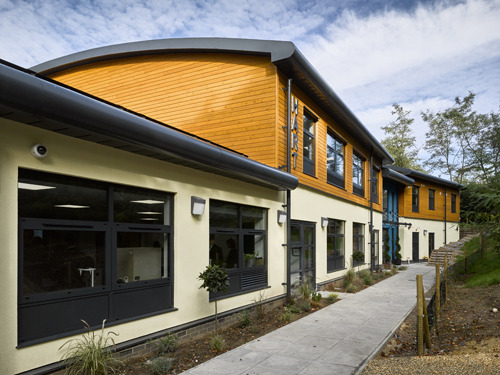 Modern school building with timber cladding and large windows next to a paved pathway.