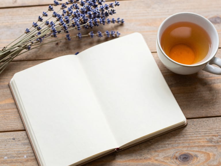 Overhead flat-lay of an open notebook, a ceramic cup of warm tea, and dried lavender branches on a rustic wooden table, soft morning daylight, shallow depth of field