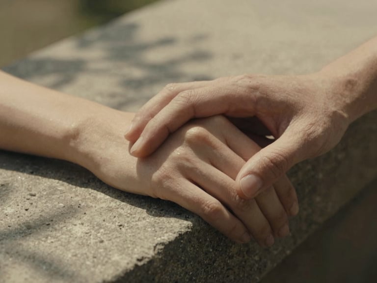 Cinematic portrait of a couple on a warm stone ledge, tight macro crop of interlocked fingers, soft dappled shade, nostalgic film grain feel.