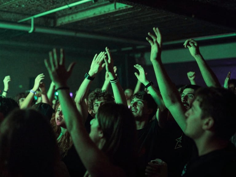 Wide low-angle shot of an underground trap concert, crowd hands raised, high-contrast neon green lighting, raw energy, 35mm film