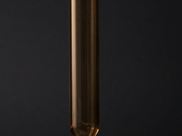 Moody close-up of a geometric glass pipe silhouette against a dark charcoal background, warm amber accent lighting, sharp focus, high-contrast, 50mm lens