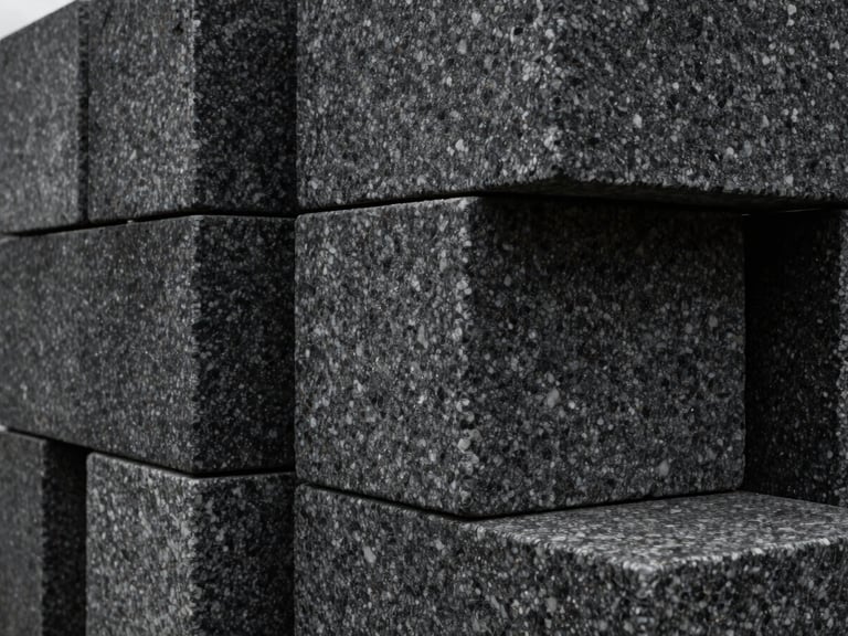 Tactile close-up of heavy dark granite blocks stacked in geometric alignment, natural overcast light, sharp textures.