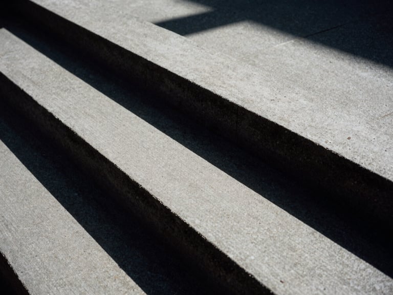 Extreme close-up of geometric concrete stairs under harsh direct sunlight, stark black shadows, high-contrast architectural detail, 35mm film grain