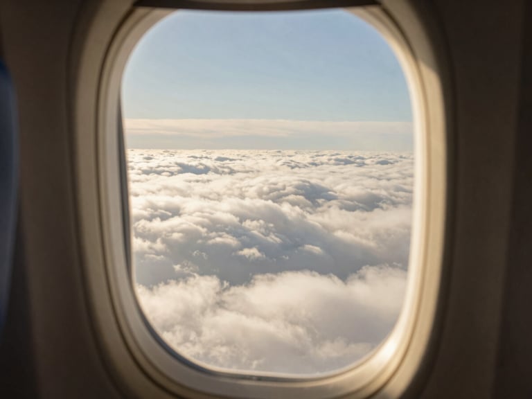 Serene window-seat view of clouds from an airplane, soft golden hour tones, shallow depth of field, warm editorial photography