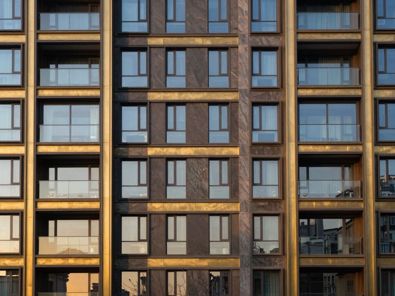Symmetric architectural shot of a luxury modern residential building facade with brass and dark stone cladding, warm golden-hour sunset reflecting in the glass windows