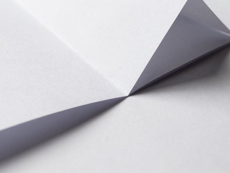 Macro close-up of sharp, folded white paper geometry casting crisp geometric shadows under hard directional daylight.
