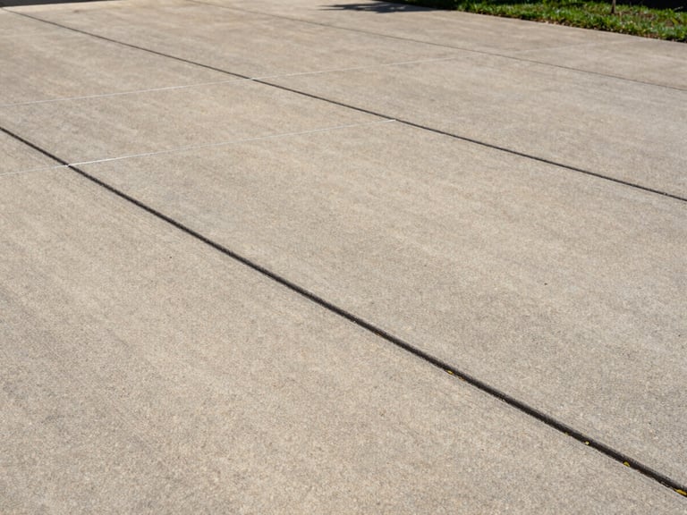 Close-up medium shot of a residential concrete driveway in Louisville, showing tight control joints and a broom-finish texture under natural daylight, sharp edge detail along the driveway border, no people