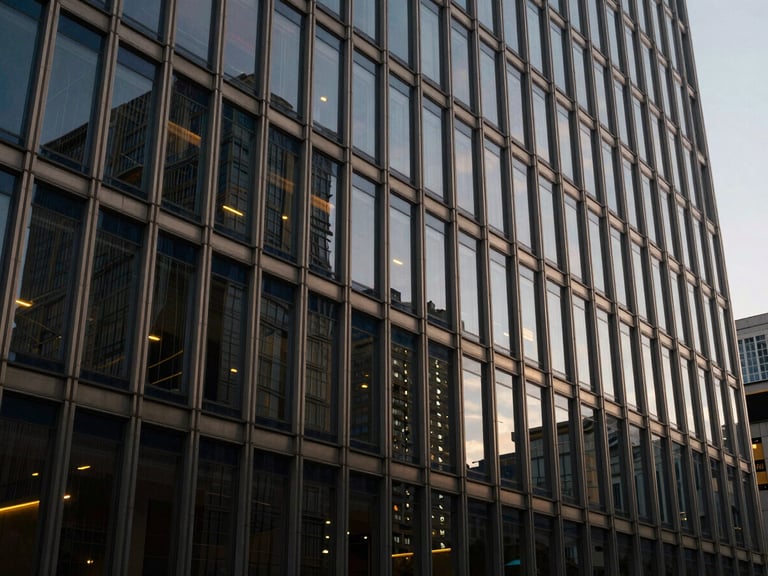 Wide architectural shot of a modern financial building facade at dusk, glass and steel reflecting city lights, deep navy and champagne tones, low contrast.