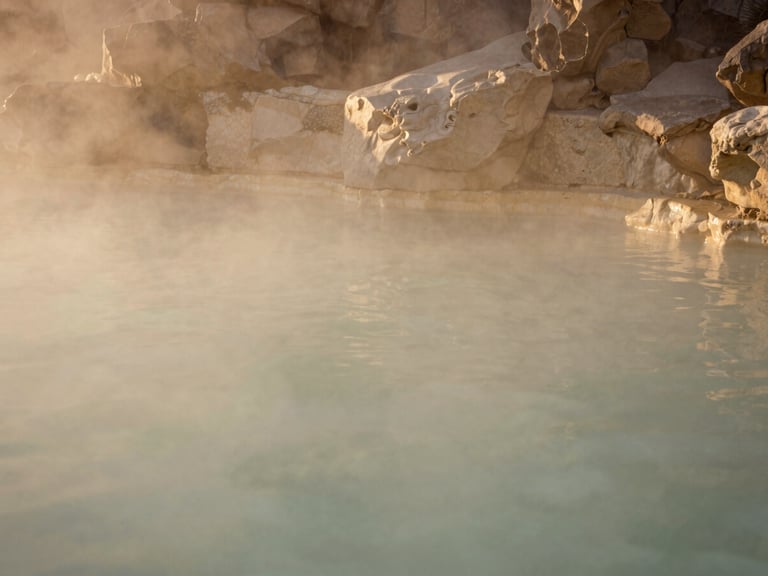 Wide shot of a serene, unpeopled subterranean thermal pool, soft golden light filtering from above, smooth stone walls, muted beige and alabaster tones. warm editorial photography, soft golden-hour light, muted beige and alabaster tones, shallow depth of field, 35mm film style.