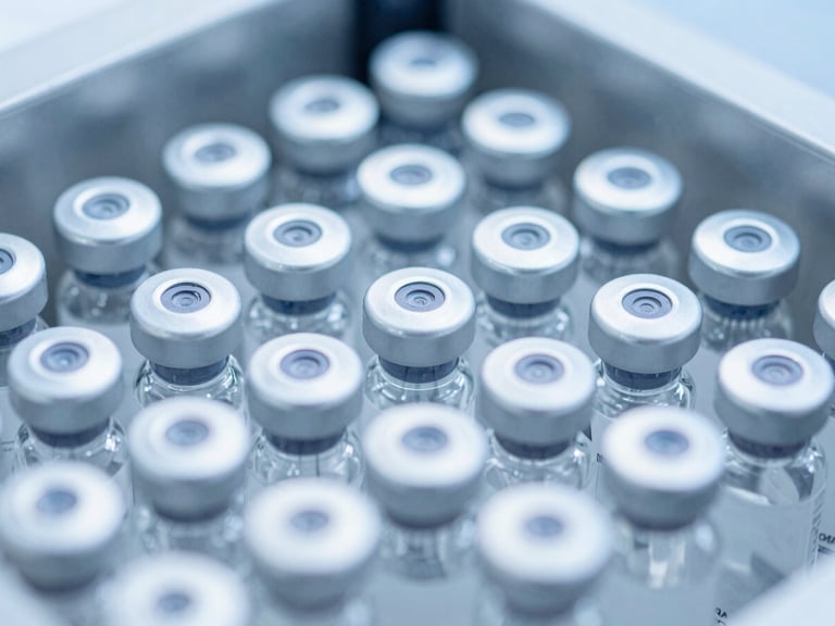 Close-up of pharmaceutical injection vials on an automated packaging line, sterile cool blue and white tones, bright high-key laboratory lighting, sharp macro focus, 35mm